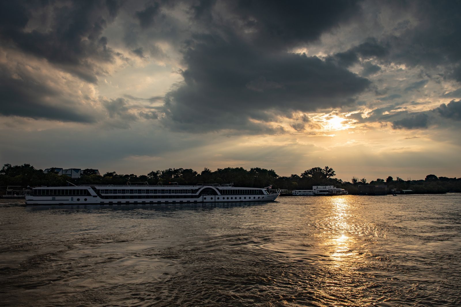 Passenger ship on a wide river under dramatic sunset clouds